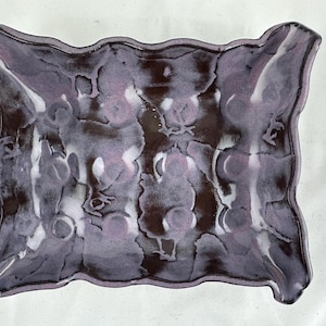 Puede incluir: Un plato de cerámica con un borde ondulado y un glaseado marmoleado morado y blanco.