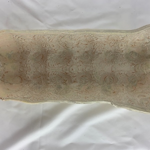 Puede incluir: Un fragmento de azulejo de cerámica con un esmalte blanco y un intrincado patrón floral en relieve de color marrón rojizo.