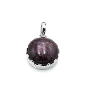 Pode incluir: Pingente redondo, roxo escuro, com um padrão em forma de estrela, emoldurado em uma moldura prateada. O pingente tem uma argola na parte superior para uma corrente. A pedra preciosa é de uma cor profunda e rica.