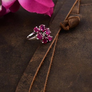 May include: A silver ring with a flower design featuring pink gemstones and a single white gemstone in the center.
