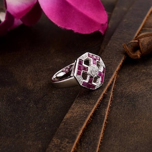 Puede incluir: Un anillo de plata con un engaste hexagonal que presenta un gran rubí rodeado de rubíes y diamantes más pequeños.