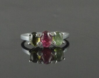 May include: A silver ring with three oval-shaped gemstones. The center stone is pink, and the stones on either side are green.