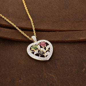 May include: A gold heart-shaped pendant necklace with a floral design. The pendant features a cluster of small flowers with red, green, and blue gemstones. The pendant is surrounded by a border of small clear gemstones.
