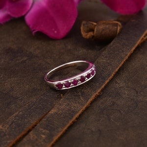 May include: A silver band ring with a row of small, red ruby stones.