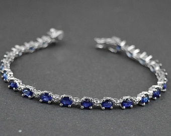 May include: A silver tennis bracelet with oval-shaped blue sapphires and small diamonds set in the metal.