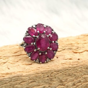Op de afbeelding: Een zilveren ring met een cluster van ovale robijn edelstenen, omringd door kleinere diamanten.
