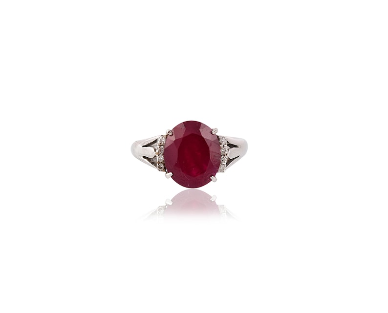 May include: A silver ring featuring a large oval ruby gemstone surrounded by smaller diamonds.