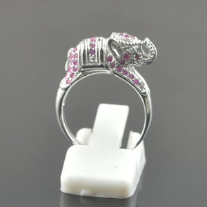 May include: A silver ring with a pink elephant design. The elephant is adorned with small pink gemstones.