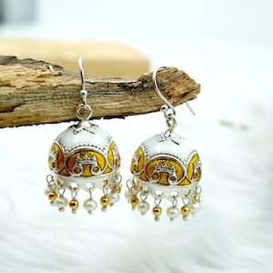 May include: A pair of silver earrings with white and gold enamel detailing. The earrings are shaped like bells with a dangling pearl and gold bead fringe.
