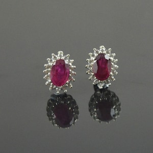 May include: A pair of ruby and diamond earrings. The earrings feature oval-shaped rubies surrounded by a halo of smaller diamonds.