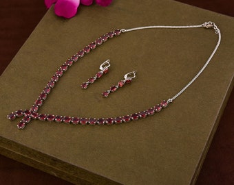 Puede incluir: Un collar y pendientes de plata con detalles de piedras preciosas rojas. El collar tiene un diseño en forma de Y con una fila de piedras preciosas ovaladas.