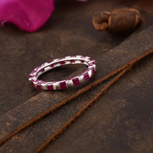 May include: A silver band ring with a row of square-shaped ruby red gemstones.