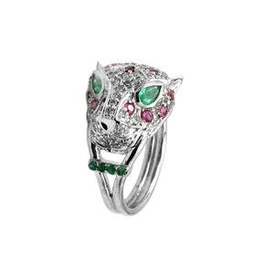 May include: A silver ring with a detailed panther head design. The panther's eyes are set with green emeralds and the head is adorned with small pink and white gemstones.