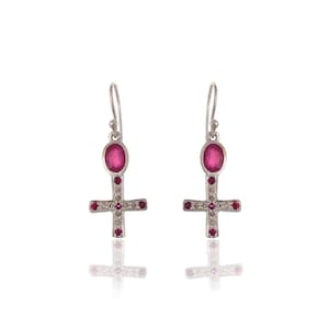 May include: A pair of silver earrings with a pink stone in the centre of each earring. The earrings are shaped like a cross with smaller pink stones on the arms of the cross.