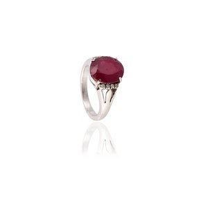 May include: A silver ring featuring a large oval ruby gemstone with a halo of smaller diamonds.