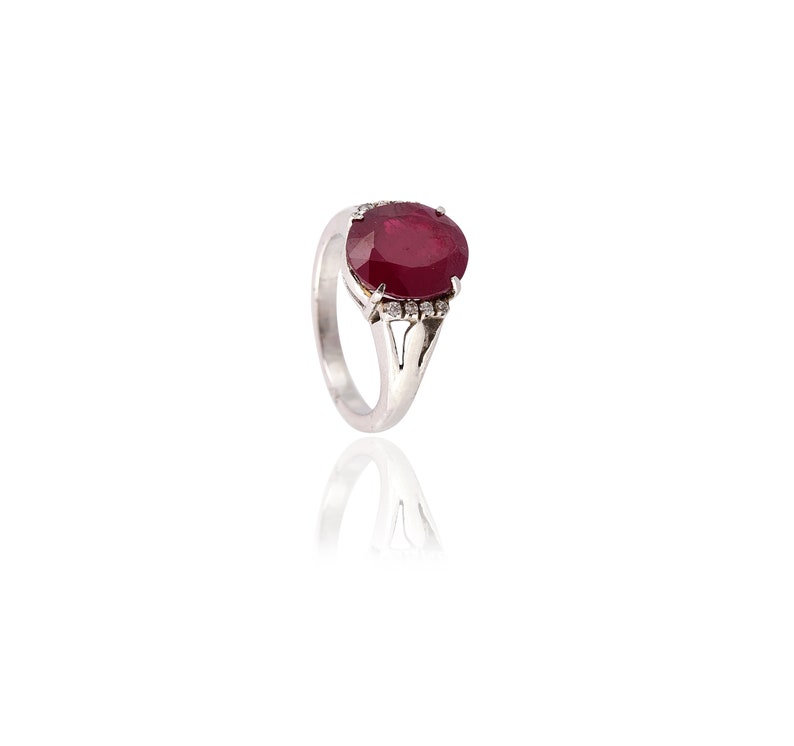 May include: A silver ring featuring a large oval ruby gemstone with a halo of smaller diamonds.