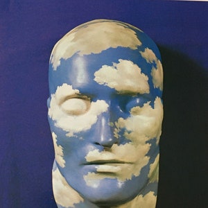 May include: A plaster sculpture of a human face with a blue and white sky painted on it. The face is painted to look like a cloudy sky.