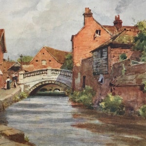 Può includere: Dipinto ad acquerello di una città europea con un ponte di pietra su un fiume. Edifici con tetti di tegole rosse e muri di mattoni costeggiano le rive. Figure che camminano lungo il sentiero. Il dipinto è firmato e datato.