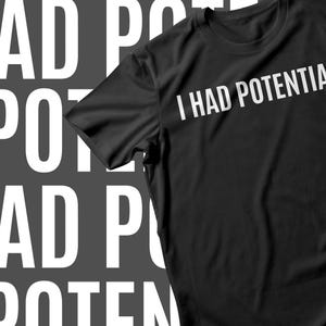 May include: Black t-shirt with the text "I HAD POTENTIAL" in white, angled across the front. The background features a repeating pattern of the words "I HAD POTENTIAL" in white against a dark gray backdrop. A casual wear item.