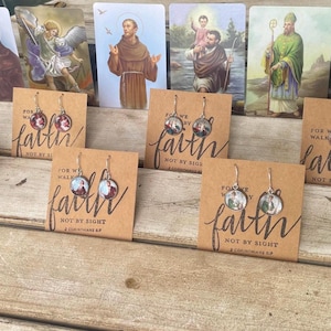 May include: Five pairs of earrings with religious images on the front. The earrings are displayed on brown cards with the text "For we walk by faith, not by sight" and a Bible verse reference.
