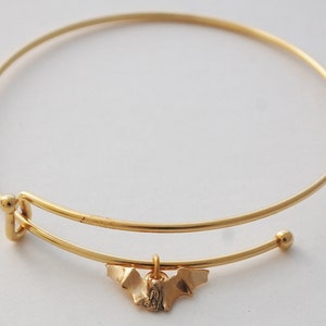May include: A gold bangle bracelet with a small bat charm hanging from it.