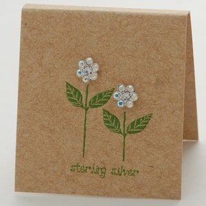 May include: A pair of sterling silver flower stud earrings with clear crystal accents on a brown card with the text "sterling silver".