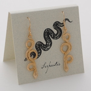 May include: Gold snake earrings on a card with the word "Serpentes" written in cursive.