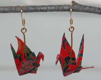 May include: A pair of red and black origami crane earrings with gold hooks. The cranes are made of patterned paper and hang from the hooks.