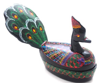 Könnte beinhalten: Eine schwarze Holzfigur eines Pfaus mit einem grün, blau und rot bemalten Design. Der Pfau hat einen langen Schwanz und einen kleinen Kopf mit einer roten Haube.