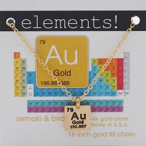May include: A gold necklace with a gold pendant featuring the chemical symbol for gold, Au, with the atomic number 79 and atomic weight 196.967. The pendant is surrounded by a white square with black text. The necklace is 16 inches long and is made of 14k gold plate. The necklace is on a white card with the text "semaki & bird" and "14k gold plate made in U.S.A." and "16 inch gold fill chain".