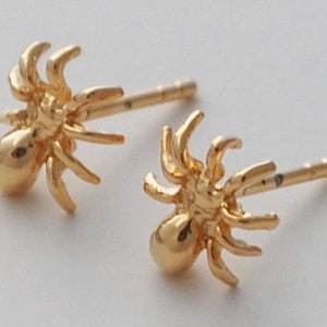 K&ouml;nnte beinhalten: Ein Paar goldene Spinnen-Ohrstecker. Die Spinnen sind detailliert und haben acht Beine.