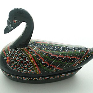 May include: A black swan-shaped decorative box with a glossy finish. The surface features intricate hand-painted feather patterns in shades of green, red, and white. The swan has a curved neck and a detailed beak, with a decorative border along the base.
