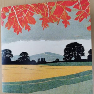 May include: A landscape print featuring a field of yellow and green with a mountain range in the background. The sky is gray, and the top of the print has red leaves.