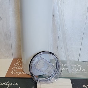 Op de afbeelding: Een witte roestvrijstalen tumbler met een doorzichtig deksel en een doorzichtige plastic rietje. De tumbler staat op een tafel met een groen en bruin gepatroneerd oppervlak. De tekst "Creativity is experimenting, taking risks, making, having fun." is zichtbaar op het oppervlak.