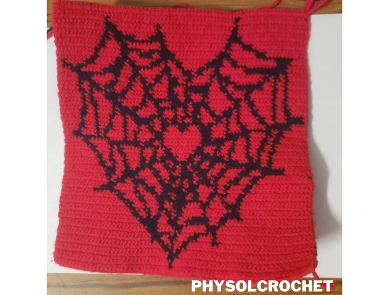 Op de afbeelding: Een rood geh&auml;keld vierkant met een zwart geh&auml;keld spinnenwebontwerp in de vorm van een hart. De tekst "PHYSOLCROCHET" is zichtbaar onderaan de afbeelding.