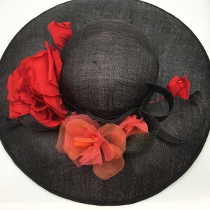 May include: A black wide-brimmed hat with a large red rose and smaller orange and red flowers.