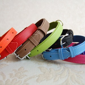 May include: A set of seven colourful leather dog collars in orange, red, brown, green, blue, pink and purple. The collars are arranged in a stack, with the orange collar at the bottom and the purple collar at the top.