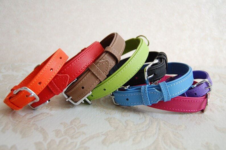 May include: A set of seven colourful leather dog collars in orange, red, brown, green, blue, pink and purple. The collars are arranged in a stack, with the orange collar at the bottom and the purple collar at the top.