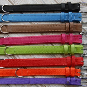 May include: Eight leather dog collars in a variety of colours, including black, blue, brown, pink, green, red, orange, and purple. Each collar has a silver buckle and a silver D-ring.