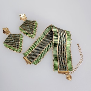 Peut inclure: Un ensemble de bijoux en perles vertes et dorées, comprenant un bracelet et des boucles d'oreilles. Les boucles d'oreilles ont un dessus en forme de fleur. Le bracelet présente un motif géométrique et un charm en forme de cœur doré.