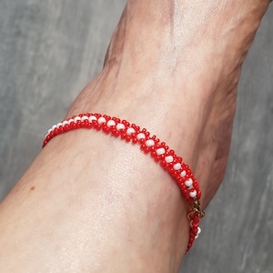 May include: Red and white beaded ankle bracelet with a gold clasp.