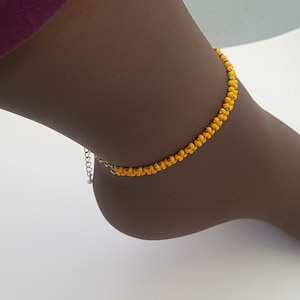 Puede incluir: Un brazalete de tobillo de cuentas amarillas con cierre de cadena plateada.