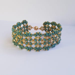 May include: A turquoise and gold beaded bracelet with a floral design. The bracelet features a magnetic clasp and is made with small, round gold beads and turquoise-colored, petal-shaped beads.