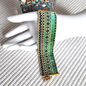 May include: A wide beaded cuff bracelet featuring a geometric pattern in shades of emerald green, black, and metallic gold. The design includes vertical columns of small seed beads and longer tube beads, finished with gold-toned metal end bars.