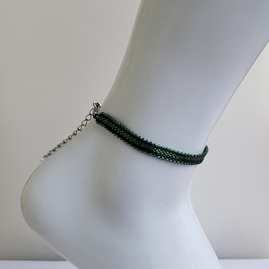 May include: A green beaded ankle bracelet with a silver chain closure.