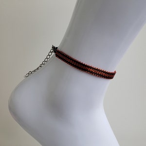 May include: A black and orange beaded ankle bracelet with a silver chain closure.