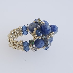 Puede incluir: Un anillo hecho con cuentas doradas y cuentas de piedras preciosas azules y transparentes.
