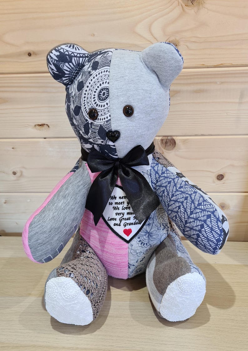 Pu&ograve; includere: Un orsacchiotto di pezza fatto di diversi tessuti, tra cui grigio, rosa e blu. L'orso ha un papillon nero e una toppa a forma di cuore con il testo "We never got to meet you. We love you very much. Love Great Nana and Grandpa".