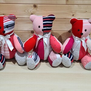 May include: Three handmade teddy bears with patchwork designs. Each bear features a mix of red, pink, and white fabrics, with striped and patterned details. They have white ribbon bows and gray sock feet.