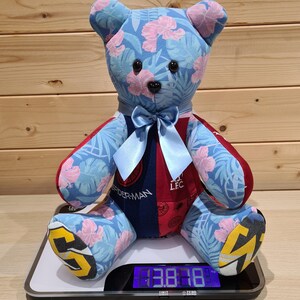 May include: A handmade teddy bear with blue fabric featuring pink floral patterns. The bear has a blue bow, and its arms and legs are red and blue. The bear is sitting on a digital scale.